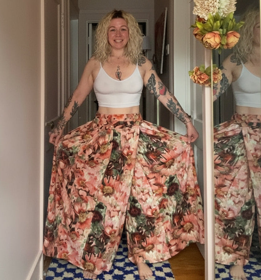 Woman wearing a white crop top and floral pants standing in a room with a mirror.